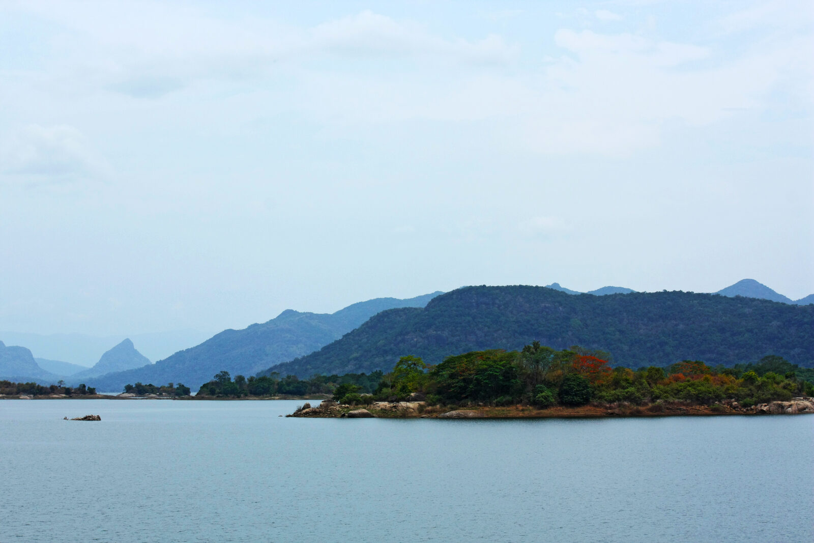 A boat crossing the Senanayake Samudraya reservoir in Gal Oya National Park, Sri Lanka, with forested hills behind