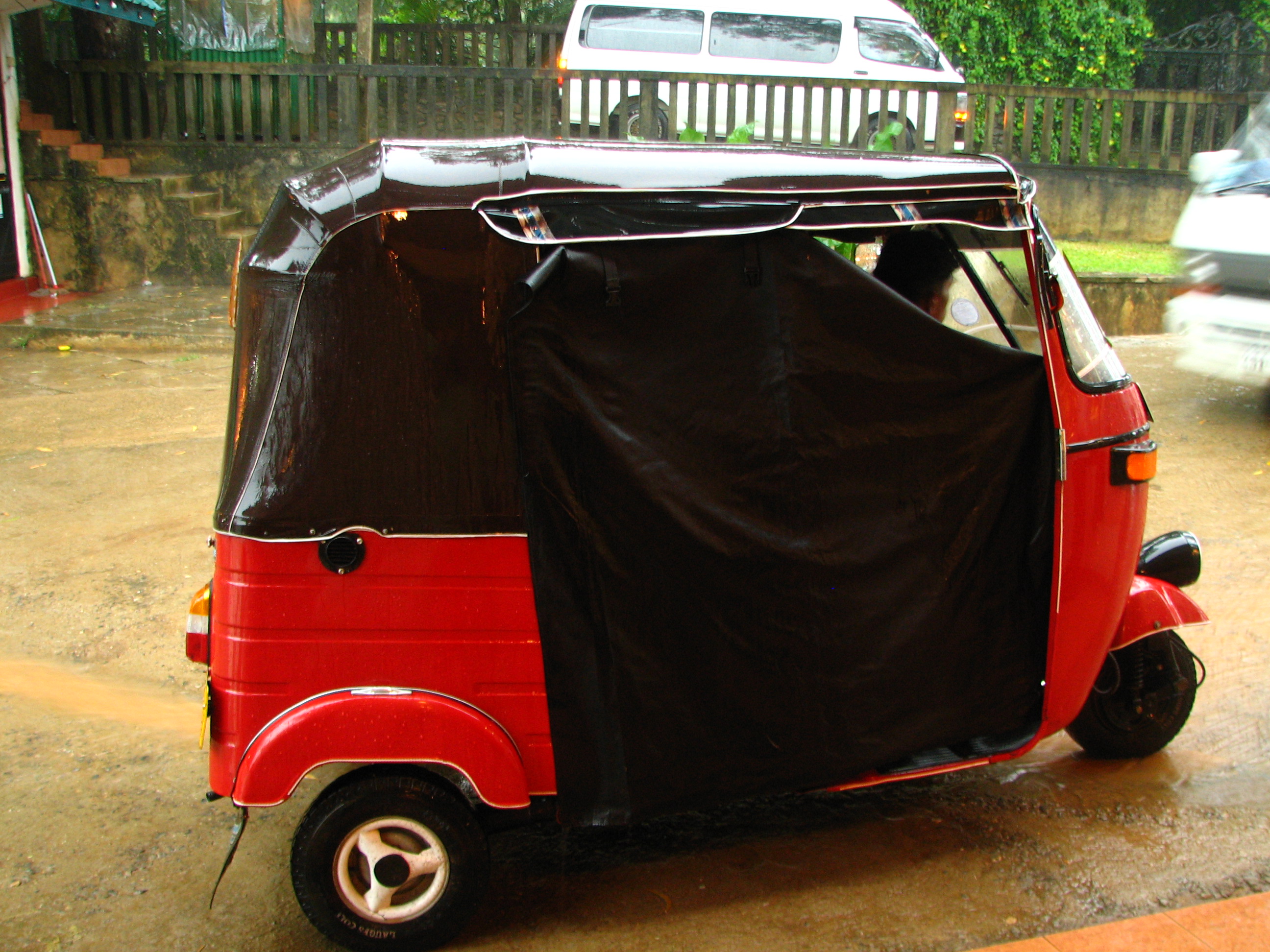 Tuk tuk parked on a Sri Lankan road ready for the rain, with tropical vegetation in the background